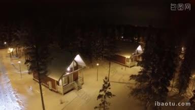 空中拍摄的乡村别墅在冬季松木在夜晚与常青树与灯笼点燃领土